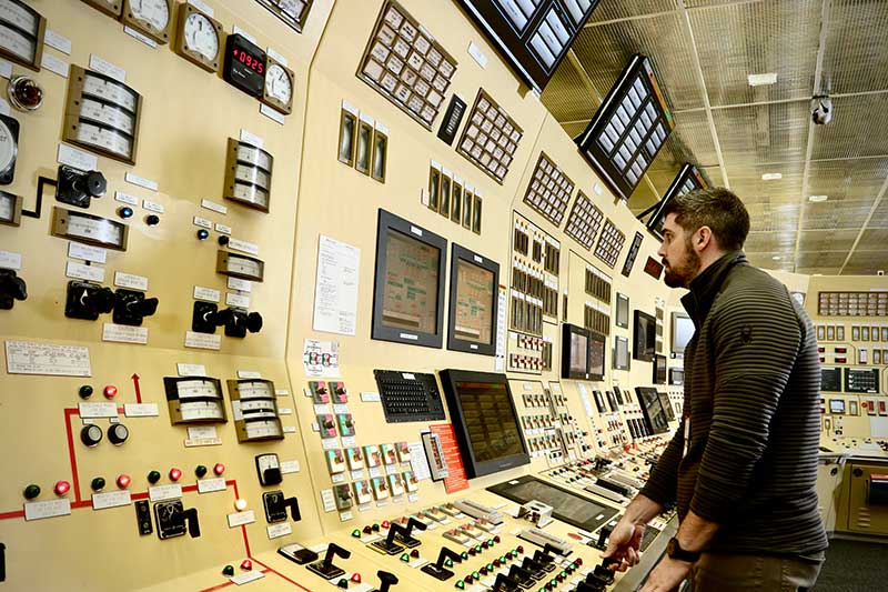Worker operating complex control panel with gauges and screens inside power plant control room