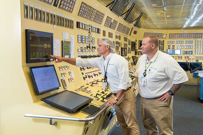 Workers reviewing data on monitor inside power plant control room with advanced control systems