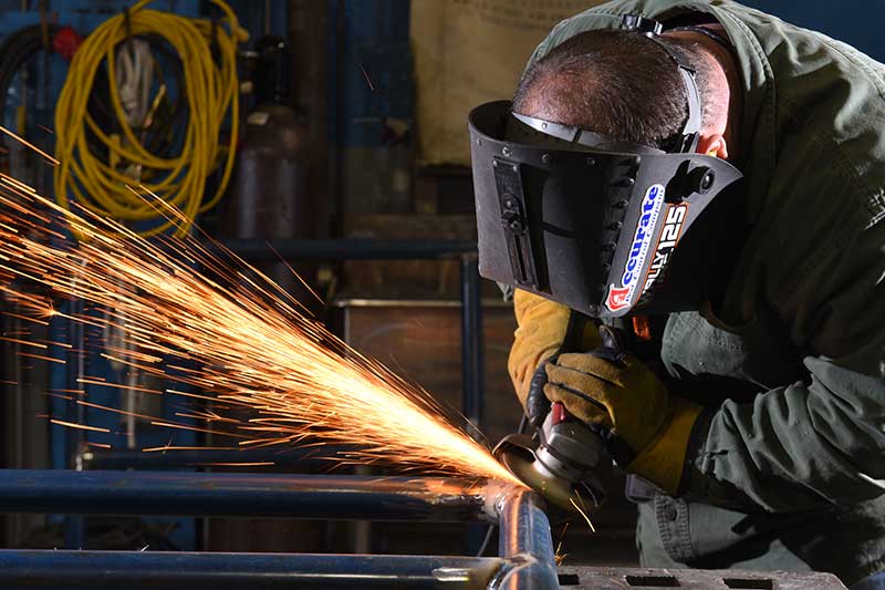 Worker using grinder on metal frame with bright sparks in an industrial workshop