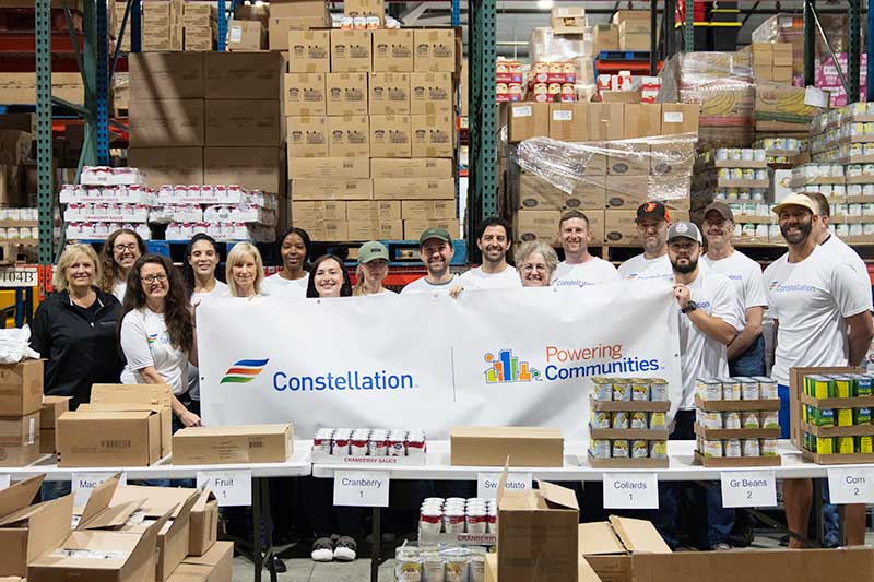 Constellation volunteers at food bank warehouse holding banner to support hunger relief