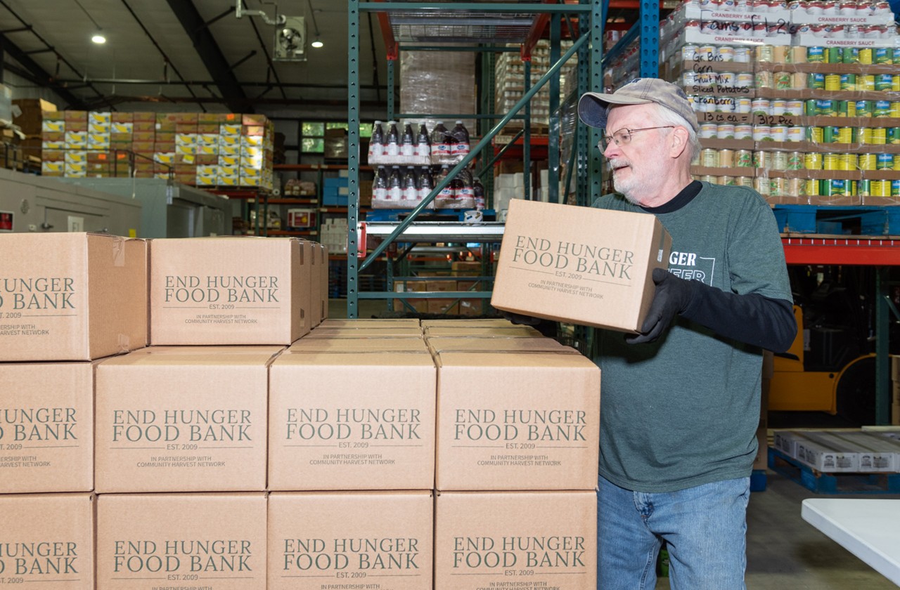 Volunteer stacking End Hunger Food Bank boxes inside a warehouse.