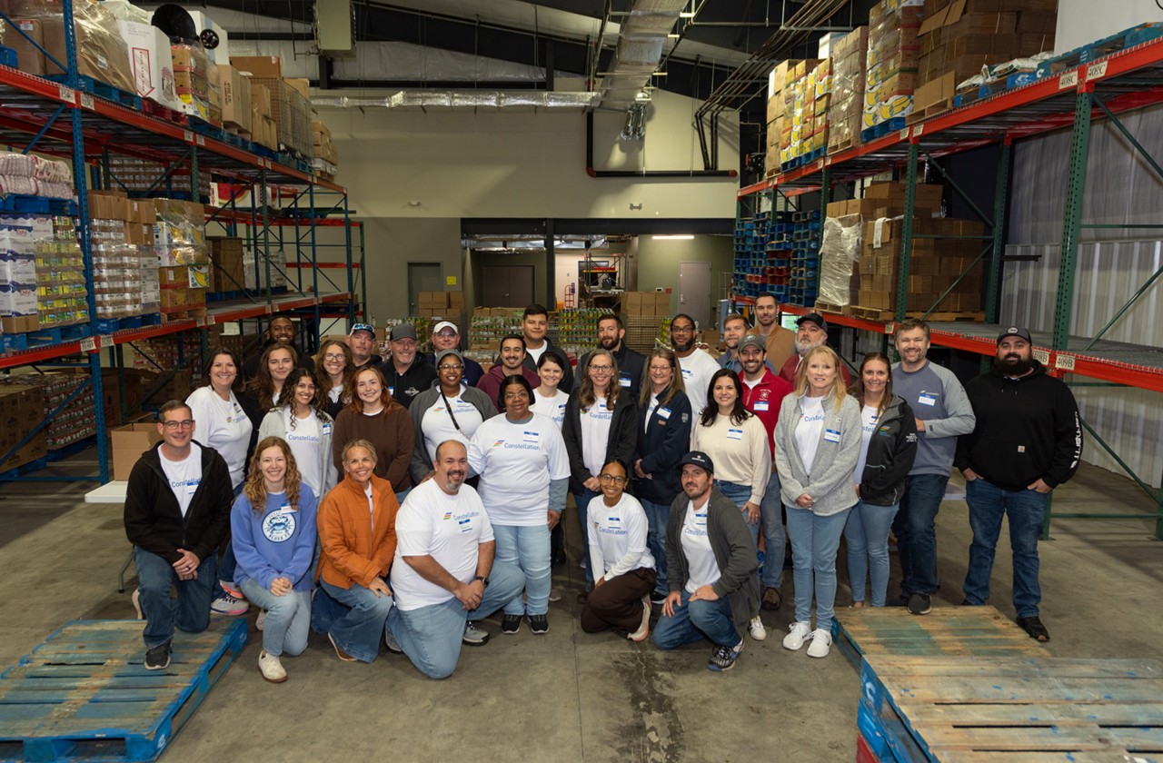 Constellation volunteers gather for a group photo inside a food bank warehouse