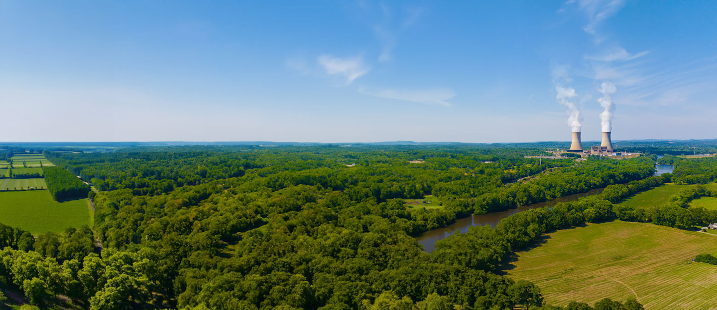 Plant with two cooling towers in the distance behind lots of greenery and land