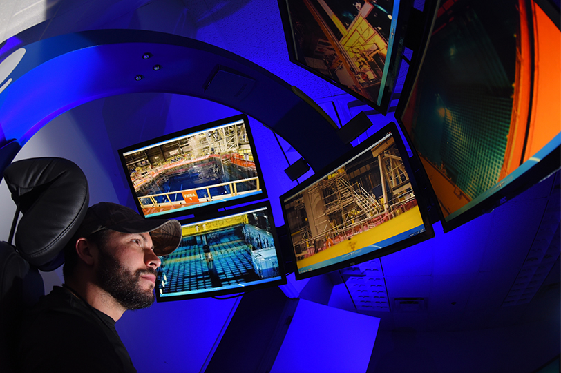 man wearing a hat surrounded by screens working in a control room