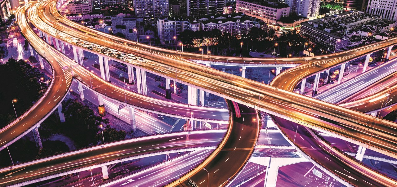 High angle view of a road intersection in downtown Shanghai, which is the conjunction of Yan'an Elevated Road and the North-South Elevated Road. Crowds of vehicles passing the elevated roads with light trails. Numerous skyscrapers are located in the futuristic megacity, illuminated by the neon lights.