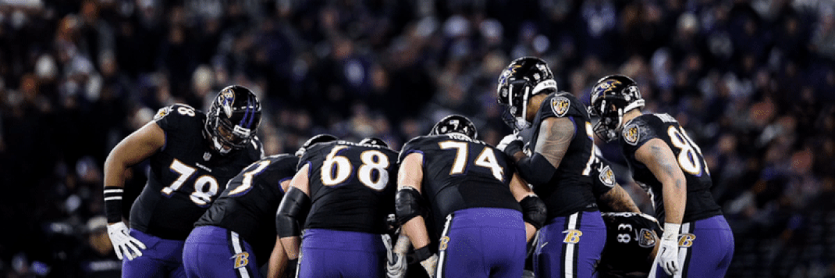 Ravens huddling on field with fans in the background 